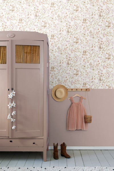 Vliestapete mit Hasen- und Blumenmotiv in einem hellen Zimmer mit rosa Kleiderschrank, hölzerner Hakenleiste und Dekoration.