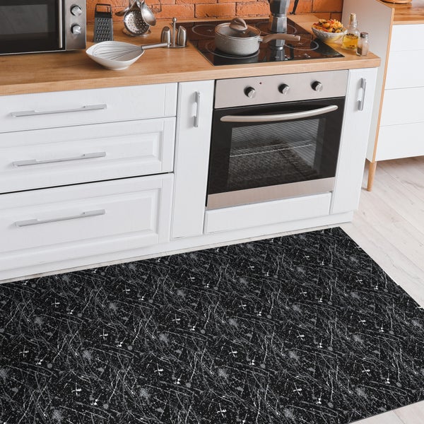 Schwarze Küchenmatte mit abstraktem Muster vor weißen Küchenmöbeln.