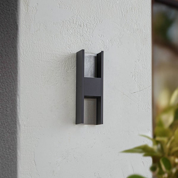 Moderne Wandaußenleuchte aus Metall in H-Form an einer weißen Hauswand montiert.