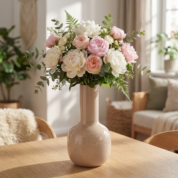 Blumenstrauß aus Pfingstrosen und Rosen in einer schlichten Vase auf einem Holztisch in einem hellen Wohnzimmer