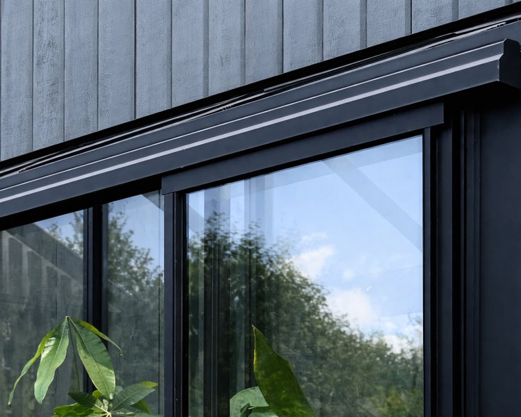 Nahaufnahme einer Glasschiebetür mit schwarzem Rahmen und oberer Führungsschiene an einer Holzfassade.