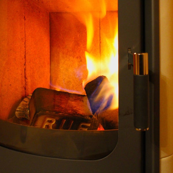 Brennende Holzbriketts mit RUF-Prägung in einem Kaminofen hinter der Glasscheibe.