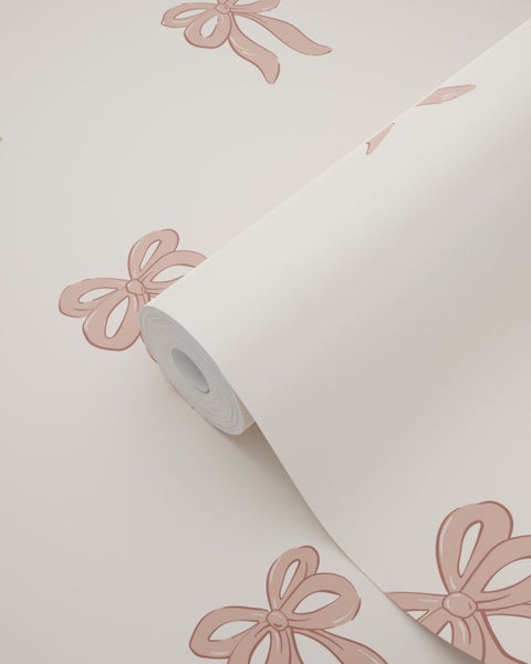 Vliestapete mit rosa Schleifen auf beige, dargestellt als teilweise abgerollte Rolle.