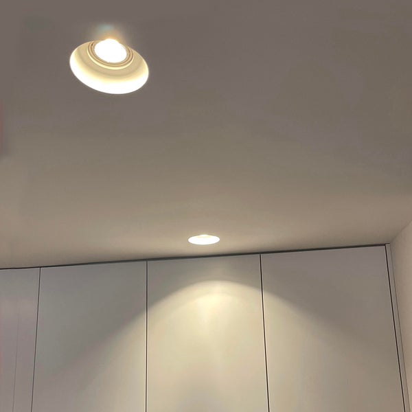 Zwei runde Einbaustrahler in einer Decke beleuchten einen Schrank von oben.