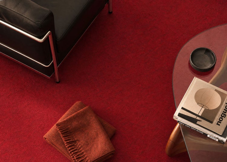 Roter Teppichboden in einem modern eingerichteten Wohnzimmer mit einem Ledersessel, einem Glastisch und Wolldecken.