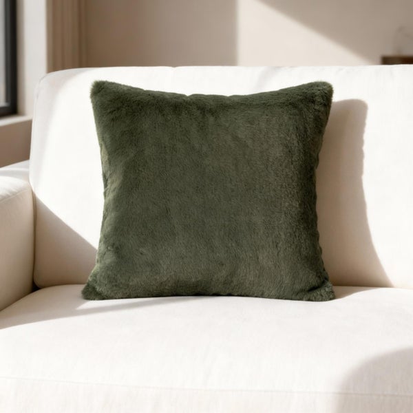 Quadratisches Kunstfellkissen in Grün auf einem hellen Sofa in einem hellen und gemütlichen Raum.