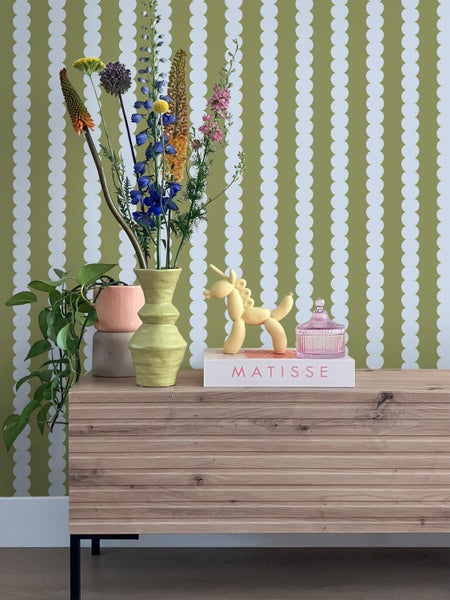 Dekorative Szene mit Blumen, Dekorationen und Holzkommode vor einer gemusterten Tapete