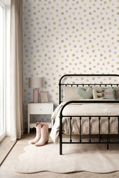 Kinderschlafzimmer mit Metallbett und einer Tapete mit Blumenmuster vor hellem Fenster mit Gardinen und Nachttisch mit Tischlampe