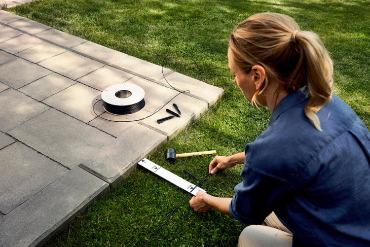 Frau verlegt Pflastersteine mit Richtschnur, Pflasterband und Gummihammer im Garten
