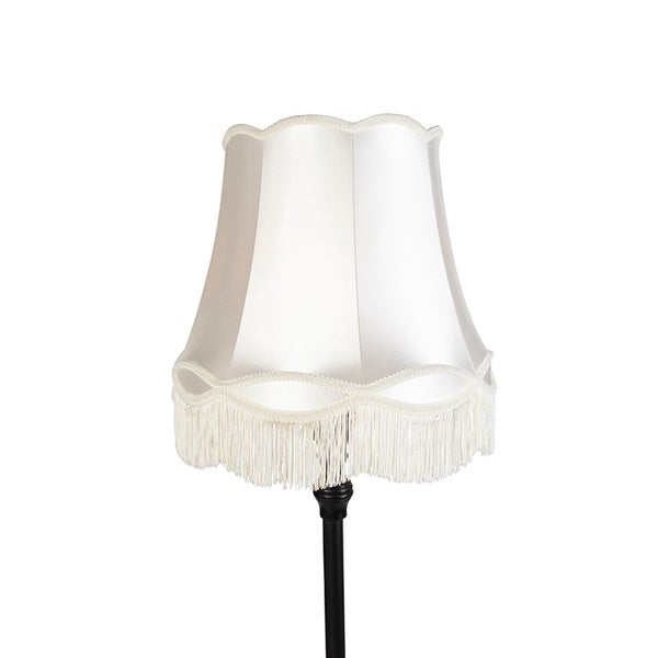 Cremefarbene Stehlampe mit Lampenschirm in Glockenform aus Stoff, Borte und Fransen.