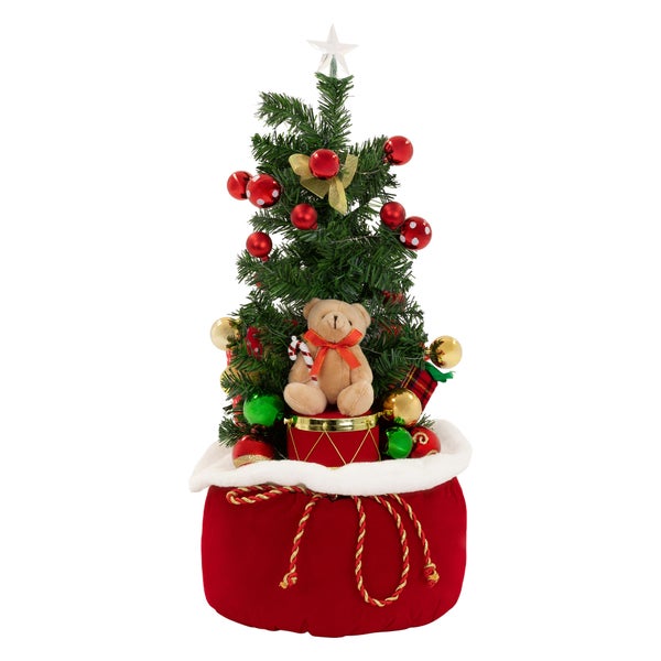 Künstlicher Weihnachtsbaum in einem weihnachtlichen Geschenkesack mit Teddybär und Kugelschmuck dekoriert