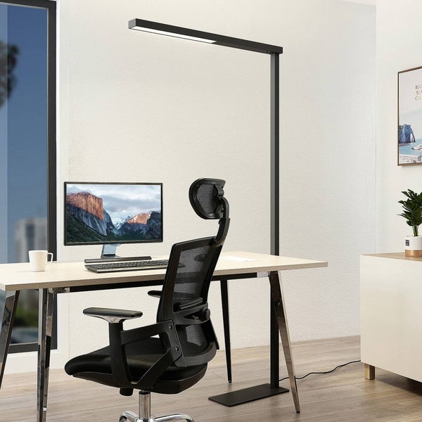 Hell gestalteter, moderner Arbeitsplatz mit einer hohen Metallstehleuchte über einem Holzschreibtisch mit Monitor und ergonomischem Bürostuhl.
