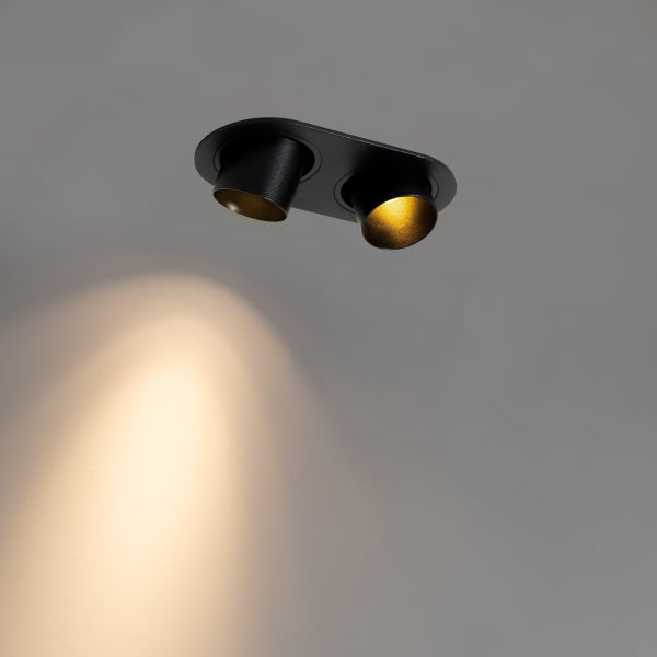 Moderner zweiflammiger Deckenstrahler in Schwarz und Gold mit warmem Lichtstrahl an der Wand.