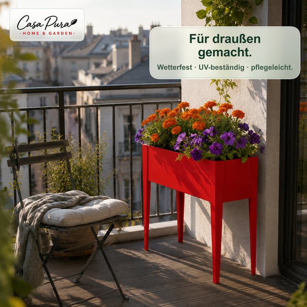 Rotes Hochbeet mit bunten Blumen auf einem Balkon neben einem Klappstuhl. Casa Pura Logo.