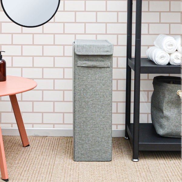 Schmaler Wäschesammler aus grauem Stoff mit Deckel in einem organisierten Badezimmer neben einem Regal mit Handtüchern.