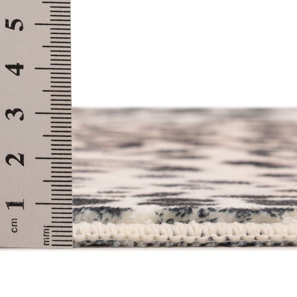 Gemusterter Teppich mit einem Lineal zur Messung der Florhöhe von circa 5 Millimetern.