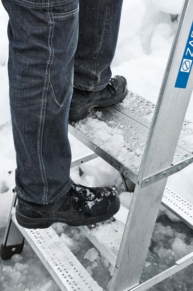 Person mit Arbeitsschuhen auf einer Leiter im Schnee