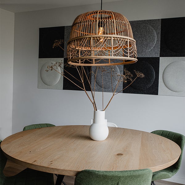 Szene mit einem Holztisch, Stühlen, einer Vase mit Zweigen, einer Rattanhängelampe und Akustikpaneelen an der Wand