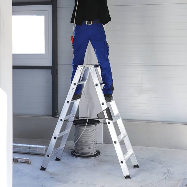 Handwerker steht auf einer stabilen Aluminium Doppelstehleiter in einem Raum während der Renovierung.