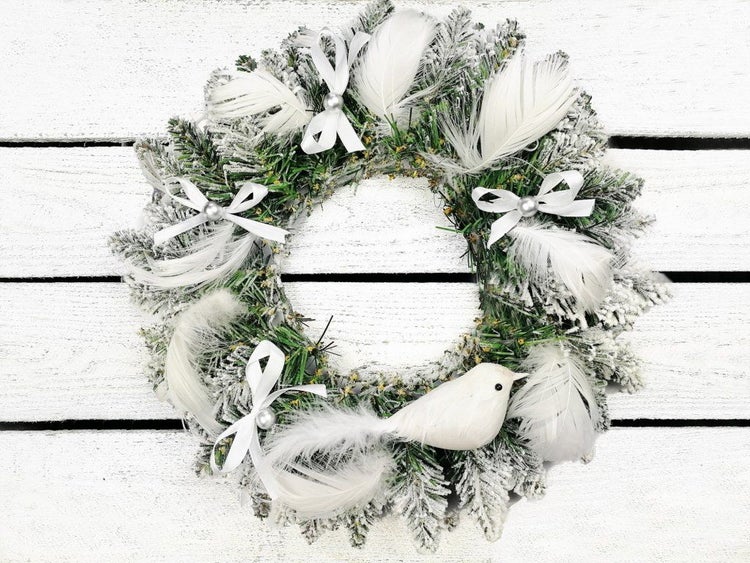 Weihnachtskranz aus künstlichen Tannenzweigen mit Kunstschnee, Federn, Schleifen und einem Vogel als Dekoration.