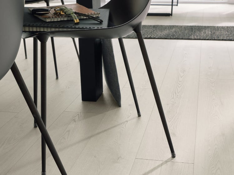 Heller Laminatboden mit Holzoptik in einem modernen Esszimmer mit schwarzen Stühlen und einem Tisch.