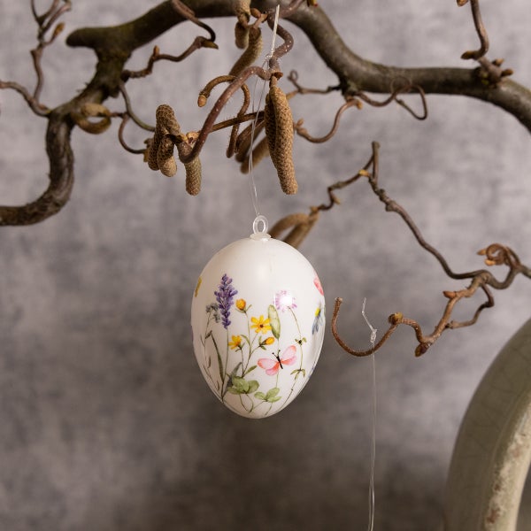 Dekoratives Osterei mit Blumenmuster hängt an einem Zweig.
