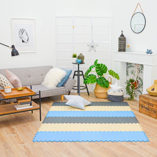 Modernes, helles Wohnzimmer mit einer gestreiften Schaumstoff-Puzzlematte auf Holzboden, einem Sofa mit Kissen, einem Dekokamin und Pflanzen.