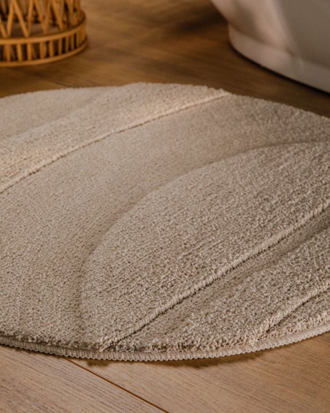 Weiche beige Badematte mit Hochflor, zusammengerollt.