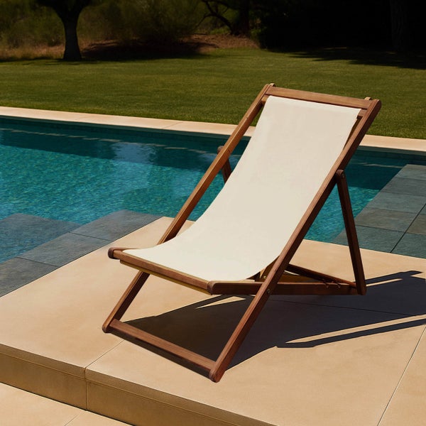 Klappbarer Liegestuhl aus Holz mit Stoffbezug auf einer Fliesenterrasse an einem Swimmingpool in einem hellen, organisierten Garten.
