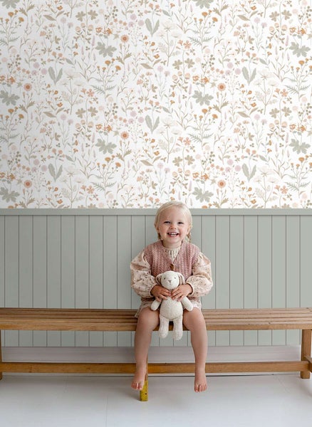 Kindersitzbank vor einer Wand mit floraler Mustertapete und vertikalem Paneel im unteren Bereich mit einem Kind und einem Kuscheltier