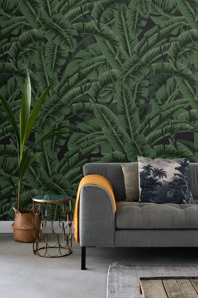 Wohnzimmer mit grauer Couch, Beistelltisch und Wandtapete mit Blättermotiv für eine tropische Atmosphäre.