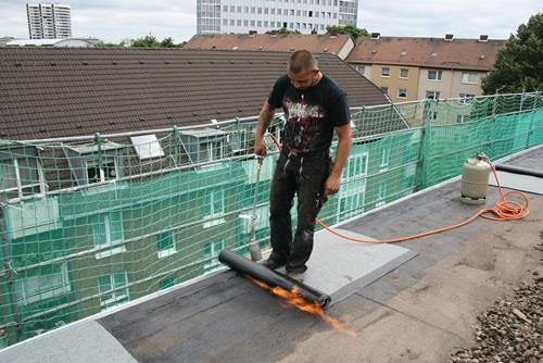 Handwerker verschweißt Bitumenbahnen mit einem Gasbrenner auf einem Dach.