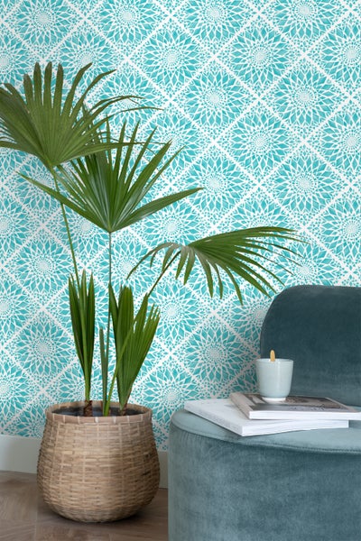 Dekoratives Zimmer mit gemusterten Tapeten, Zimmerpflanze in einem Korb und einem Hocker mit Büchern.