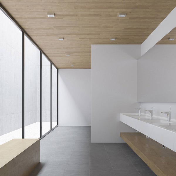 Modernes, helles Badezimmer mit Deckenpaneelen in Holzoptik, grauen Bodenfliesen, langem weißem Waschtisch und drei verchromten Armaturen.
