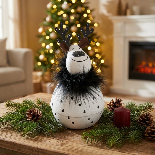 Weihnachtsdekoration Rentierfigur aus Keramik mit Geweih und Federkragen als Tischschmuck auf einem Holztisch mit Tannenzweigen und Zapfen