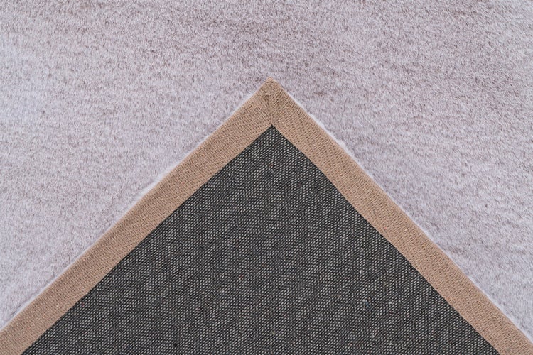 Detailansicht eines flauschigen Teppichs mit gewebter Einfassung und strukturierter, rutschhemmender Rückseite.