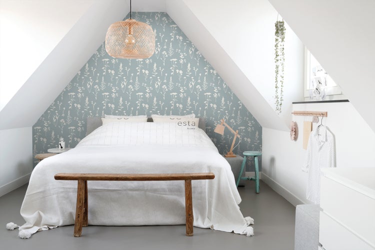 Schlafzimmer im Dachgeschoss mit Bett, Holzbank und floraler Tapete