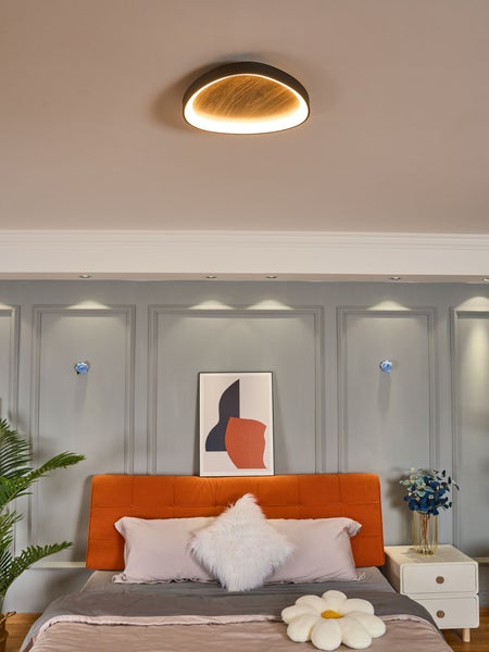 Moderne runde Deckenleuchte in Holzoptik und Schwarz in einem hellen Schlafzimmer über einem Bett mit orangefarbenem Kopfteil.