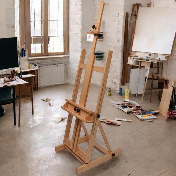 Holzstaffelei in einem hellen Atelier mit Farbtuben und anderen Malutensilien.