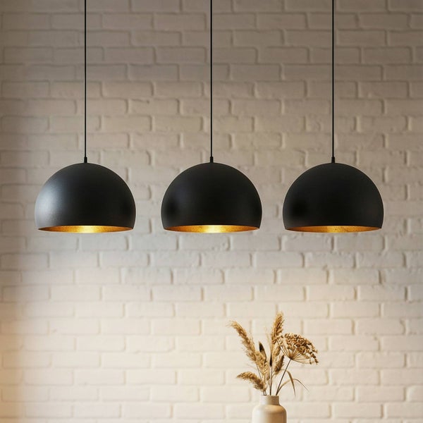 Drei schwarze Pendelleuchten mit goldfarbener Innenseite vor einer Ziegelwand