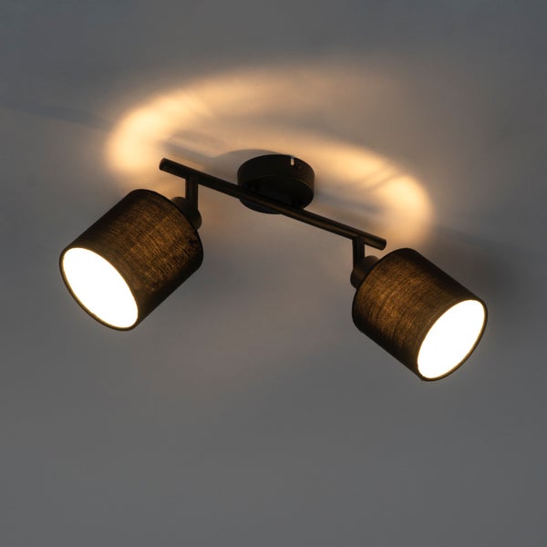 Deckenleuchte mit zwei verstellbaren Strahlern, schwarzem Metallgestell und dunklen Stoffschirmen, eingeschaltet mit warmem Licht.