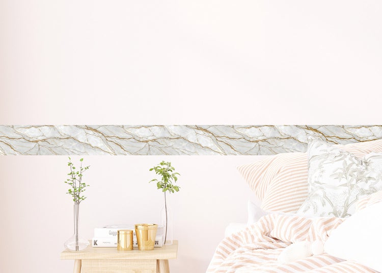 Tapetenbordüre mit Marmor-Muster und Goldadern an einer hellen Wand über einem Bett im Schlafzimmer.