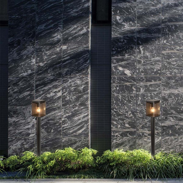 Zwei Gartenleuchten beleuchten einen Außenbereich mit Steinmauer und Pflanzen.