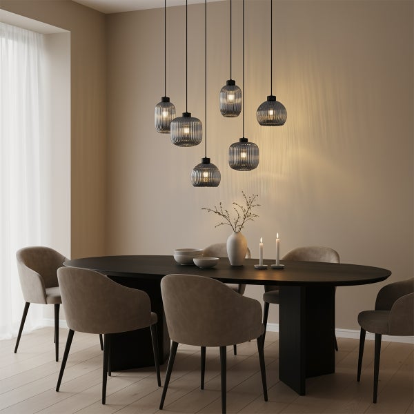 Modernes Esszimmer mit sechs Pendelleuchten mit geriffelten Glasschirmen in verschiedenen Höhen über einem dunklen ovalen Tisch und beigen Stühlen.