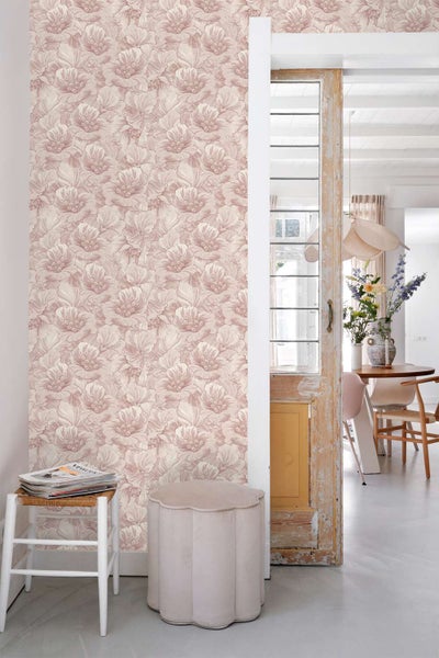 Wohnraum mit einer Wand, die mit einer floralen Mustertapete tapeziert ist, neben einer rustikalen Holztür und einer Essecke im Hintergrund.