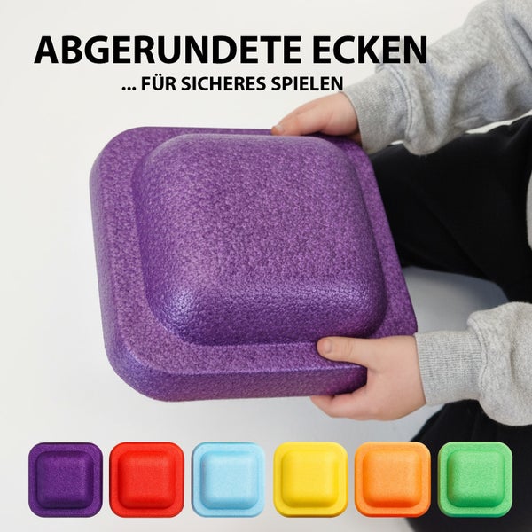 Quadratischer, violetter Spielbaustein mit abgerundeten Ecken für sicheres Spielen wird von einem Kind gehalten, darunter weitere Spielbausteine in Rot, Blau, Gelb, Orange und Grün