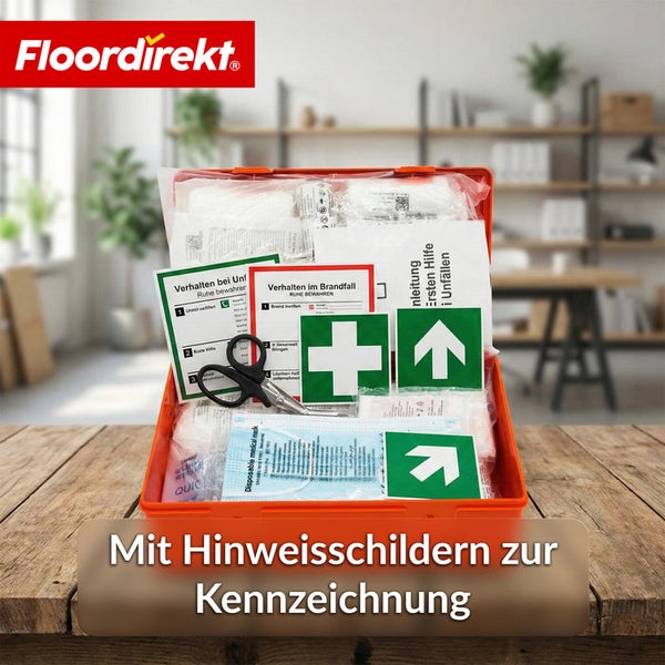 Geöffneter Erste-Hilfe-Koffer mit Verbandsmaterial, Schere, Masken und Hinweisschildern zur Kennzeichnung auf einem Holztisch. Floordirekt Logo.