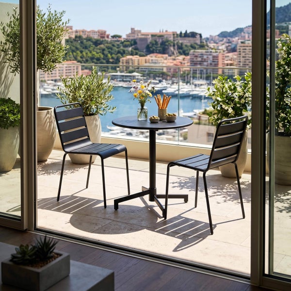 Modernes Balkon-Set mit rundem Metalltisch und zwei Stühlen mit Querstreben auf einem hellen Balkon mit Pflanzen und Blick auf den Hafen.