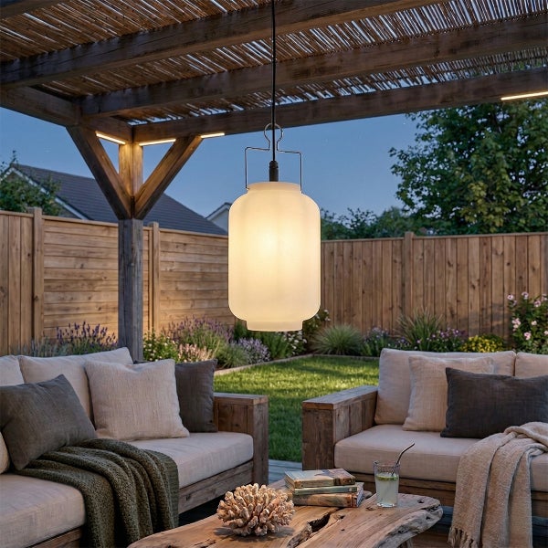 Moderne Lounge im Außenbereich unter einer Holzpergola bei Dämmerung, mit einer großen Pendelleuchte aus Milchglas und Holzmöbeln.