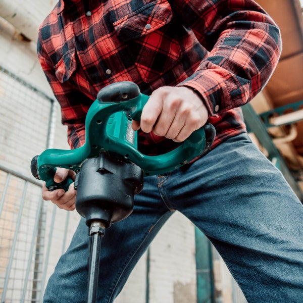 Person bei der Arbeit mit einem elektrischen Rührwerk zum Mischen von Baustoffen auf einer Baustelle.